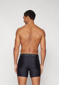 Black boxer shorts with an elastic waistband featuring a logo, fitted design, and smooth texture, viewed from the back on a model.