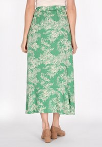 Fustă maxi verde cu un model floral alb, talie elastică, textură netedă și un croi fluid, asortată cu pantofi cu toc bloc bej.