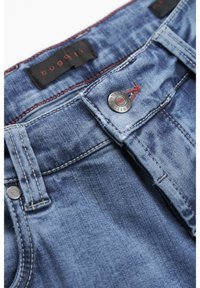 Jeans dżinsowe w niebieskim odcieniu, z kontrastującymi czerwonymi szwami, metalowym zapięciem na guzik oraz czarną metką z napisem "bugqti" w pobliżu pasa.