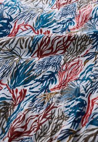 Tela con un patrón repetido de formas similares a corales en azul, rojo y marrón sobre un fondo blanco; textura suave, diseño nítido.