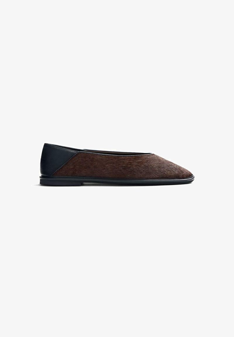 Zapato plano con un empeine marrón texturizado similar al cabello y un tacón de cuero negro liso. Presenta una punta redondeada y un diseño minimalista.