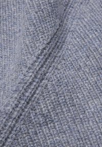 Tessuto lavorato a maglia grigio chiaro con una texture a coste e una leggera piegatura che crea ombre e profondità.