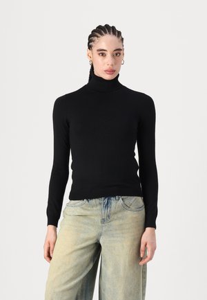 Un pull à col roulé noir en tissu lisse, silhouette ajustée, manches longues et poignets côtelés, associé à un pantalon en denim clair à jambes larges.