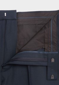 Pantaloni navy con zip frontale e interno in tessuto liscio; includono un gancio in metallo e dettagli di cucitura blu a contrasto.