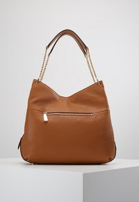 Sac hobo en cuir marron avec une finition texturée, des anses en chaîne dorée et une poche zippée à l'avant. Forme douce et courbée avec des bords inférieurs arrondis.
