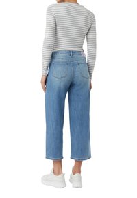 Hellblaue weit geschnittene Jeans mit hoher Taille, ausgestattet mit einem ausgewaschenen Finish und einem pinken Etikett auf der Gesäßtasche, kombiniert mit einem grau gestreiften Oberteil und weißen Sneakers.