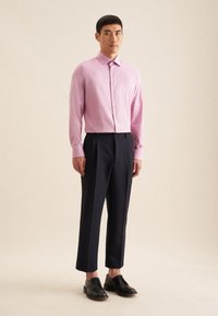 Camicia a maniche lunghe rosa chiaro con colletto e bottoni, abbinata a pantaloni formali blu scuro e scarpe nere stringate.
