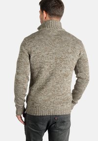 Maglione a maglia con colletto alto, motivo marrone e beige texturizzato, polsini e orlo a coste, indossato con jeans scuri, visto da dietro.