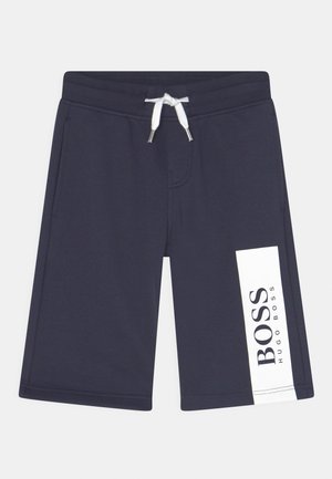 Granatowe krótkie spodenki do kolan z białym sznurkiem w pasie oraz białą pionową metką na lewej nogawce z napisem „BOSS HUGO BOSS.”