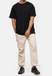 Schwarzes Baumwoll-T-Shirt mit Rundhalsausschnitt, kombiniert mit hellbeigen Hosen mit elastischem Bund und schwarzen Sneakers. Einfaches Design und lockere Passform.