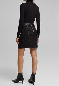 Maglia nera aderente con collo a serafino abbinata a una mini gonna nera scintillante con zip sul retro e stivaletti neri alla caviglia.
