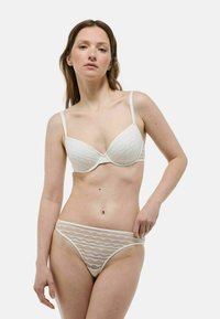 Ensemble de lingerie blanche comprenant un soutien-gorge à armatures avec un motif en vagues et un string assorti, fabriqué dans un tissu doux et transparent avec des bretelles ajustables.