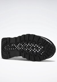 Semelle en caoutchouc noire d'une chaussure Reebok avec des sculptures profondes et des crampons ronds conçus pour l'adhérence sur diverses surfaces.