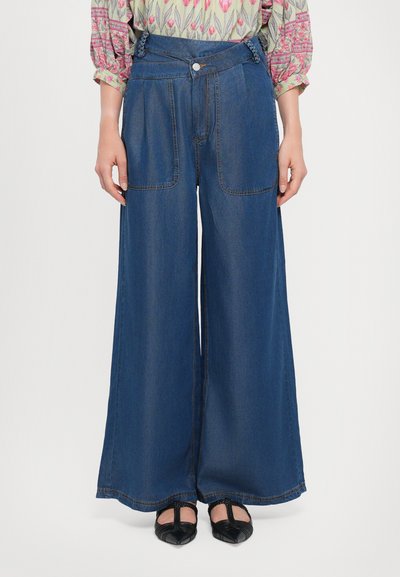 Brede denimbroek in donkerblauw, met grote voorzakken en een gladde afwerking. De tailleband heeft een knoopsluiting en gestikte details.