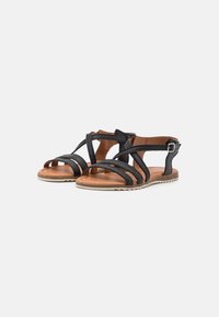 Sandales noires avec des brides croisées et fermeture à boucle, dotées d'une semelle intérieure beige et d'une semelle extérieure en caoutchouc texturé pour une meilleure adhérence.