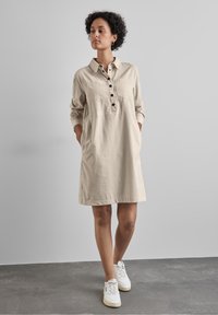Robe boutonnée beige en coton au style décontracté, avec deux poches poitrine, des manches longues et un ourlet droit.