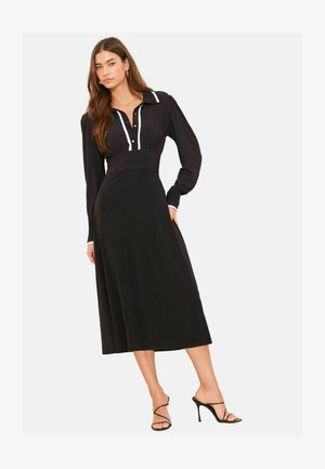 Fekete midi ruha, testhez álló felsőrésszel, hosszú ujjakkal és gombos elülső résszel. Fehér részletek a galléron és az ujjszegélyen.