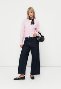 Cardigã rosa de malha canelada, calças largas de ganga azul-escura, sapatos planos pretos e um lenço preto com bolinhas. Inclui uma mala preta.