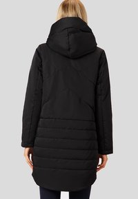 Černá prošívaná bunda s kapucí, s prošívaným vzorem a delším zadním dílem. Hladká textura, teplý materiál a jednoduchá konstrukce.