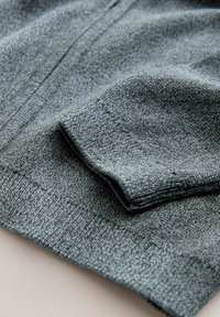 Close-up van de opgevouwen grijze gebreide trui-sleeve die ribbels aan de mouwen en een gestructureerde stof laat zien.