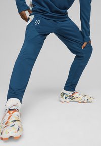 Pantalones deportivos azul oscuro con un diseño texturizado y acentos claros, combinados con zapatillas coloridas que presentan patrones abstractos y picos naranjas.