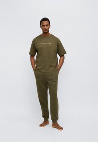 Πράσινο ελιάς βαμβακερό μπλουζάκι με κοντά μανίκια και λογότυπο, συνοδευόμενο από ταιριαστό παντελόνι jogger με ελαστικά τελειώματα και άνετη εφαρμογή.