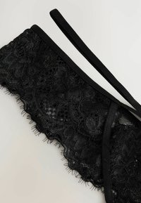 Lingerie in pizzo nero con motivi floreali, caratterizzata da una texture trasparente, bordi in raso e spalline regolabili.