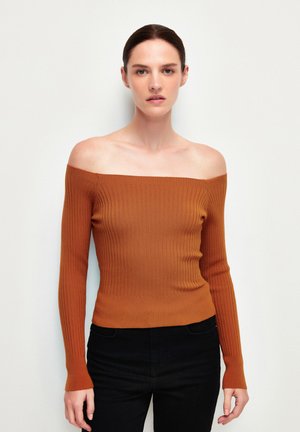 Off-the-shoulder ribbeltrui in roestkleur, met lange mouwen, een getailleerd ontwerp en een zachte textuur. Gepaard met donkere jeans.