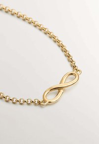 Collar de oro con cadena de eslabones y un colgante en forma de infinito. El colgante es liso y pulido, lo que realza su calidad reflectante.