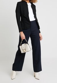 Czarna marynarka w kropki o dopasowanym kroju, zestawiona z granatowymi spodniami o szerokich nogawkach. Uzupełniona białą torebką i beżowymi botkami na obcasie.