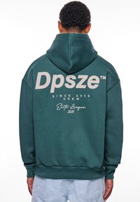 Mørkegrønn hettegenser med kengurulomme, med stor lys grå tekst: "Dpsze" og "Since 2020 Crew" på ryggen. Løs passform.