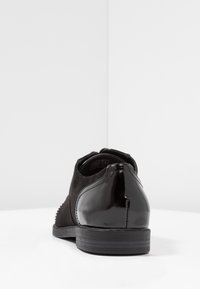 Chaussure pour homme en daim noir et cuir verni avec une surface lisse et une légère texture, dotée d'un petit talon et d'un bout arrondi.