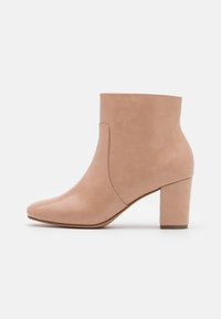 Stivali alla caviglia beige con una finitura in pelle sintetica liscia, punta affusolata e tacco a blocco. Presentano cuciture minime e un design slip-on.