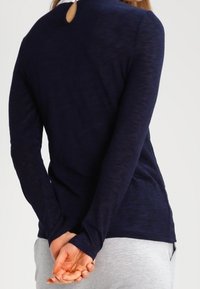 Marinblå långärmad topp med texturerad finish, med en nyckelhålsdetalj bak och en avslappnad passform med rundad fåll.