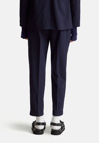 Marynarski garnitur w paski, składający się z marynarki i spodni, wykonany z tkaniny tkanej. Spodnie mają podwinięte mankiety, w zestawieniu z białymi skarpetkami i czarnym obuwiem.