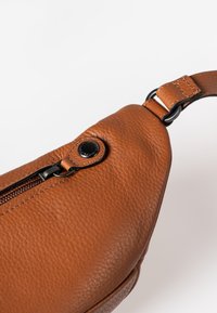Bruine leren schoudertas met een gestructureerde afwerking, voorzien van een ritsluiting en een metalen drukknoopdetail. Inclusief verstelbare schouderband.