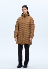 Bruine pufferjas met capuchon, voorzien van een rits en een chevron-quilted ontwerp. Gekocht over zwarte broek en laarzen. Zachte textuur.