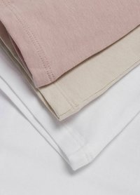 Trois t-shirts pliés en coton, de couleur rose clair, beige et blanc. Chacun a une texture lisse et des coutures visibles le long des bords.