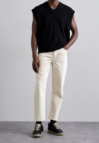 Suéter negro sin mangas de punto, diseño de cuello en V, combinado con unos jeans rectos color crema y zapatillas negras con cordones crema y suelas texturizadas.