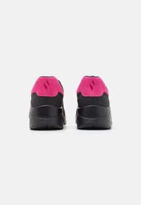 Black athletic shoes with a pink suede heel accent, featuring a textured rubber sole and a streamlined design for support and comfort.