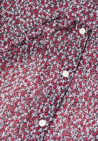 Gros plan d’un tissu à petit motif floral rouge et blanc, détail volanté et boutons blancs sur un matériau léger.