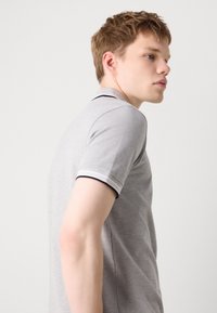 Γκρι πόλο μπλούζα με μαύρη και λευκή ριγωτή κολάρο και μανίκια, διαθέτει κοντά μανίκια και λεία υφή. Το μοντέλο εμφανίζεται σε προφίλ.