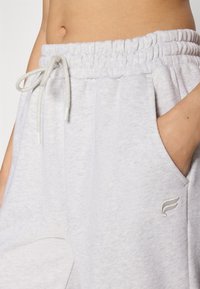 Pantaloni sportivi grigi chiari con una finitura testurizzata, dotati di una vita elastica, cordino, tasche laterali e una piccola accentatura logata.