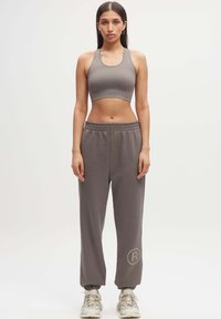 Grijze activewear set bestaande uit een cropped sportbeha en losse sweatpants met een elastische tailleband. De broek heeft een ronde logo-accent.