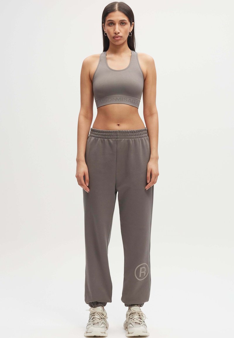 Grijze activewear set bestaande uit een cropped sportbeha en losse sweatpants met een elastische tailleband. De broek heeft een ronde logo-accent.