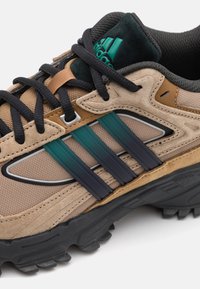 Hnědé semišové a síťované tenisky s černými tkaničkami, zelen�ými a námořnickými pruhy, silnou černou podrážkou a polstrovaným límcem. Obsahuje reflexní detaily.