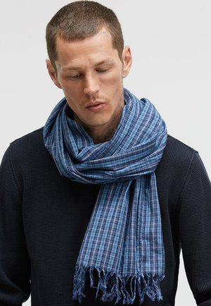 Blue plaid scarf made of lightweight fabric with fringed edges, draped around the neck, featuring varying shades of blue.