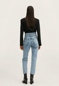 Jeans de tiro alto en un tono azul claro con una tela texturizada, presentando una cinturilla elástica fruncida, combinados con una blusa negra de manga larga y botas negras de tacón.
