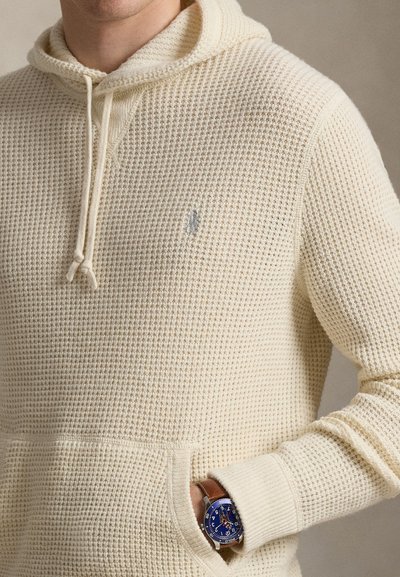 Kermansävyinen neulottu huppari, jossa on teksturoitu, vohvelikuvio, etutasku ja kiristysnauhallinen huppu sekä pieni kirjailtu logo.