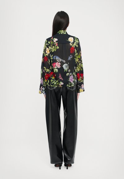 Sheer black blouse with vibrant floral print, long sleeves, and a collar. Paired with high-waisted, sleek black faux leather pants.